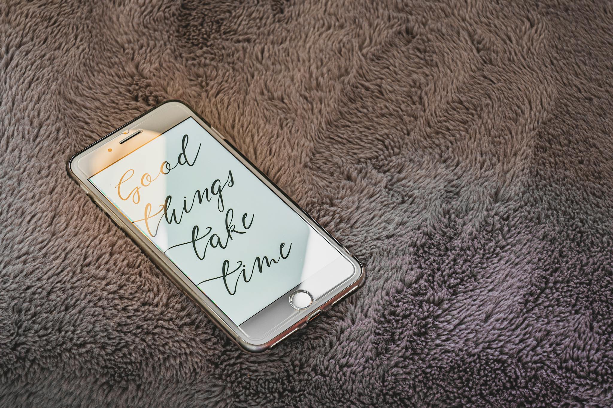 Smartphone on soft blanket displaying 'Good things take time' text.
